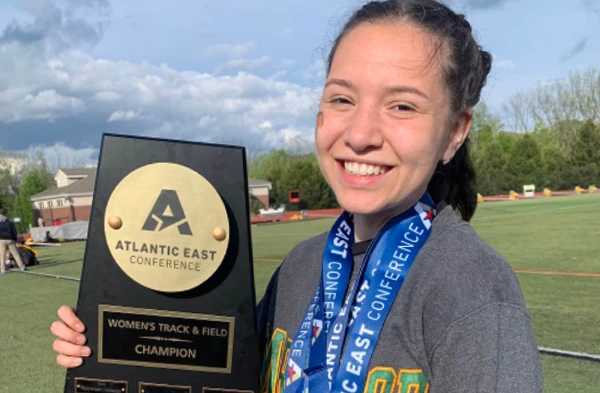 A female student-athlete holding onto an AEC trophy.